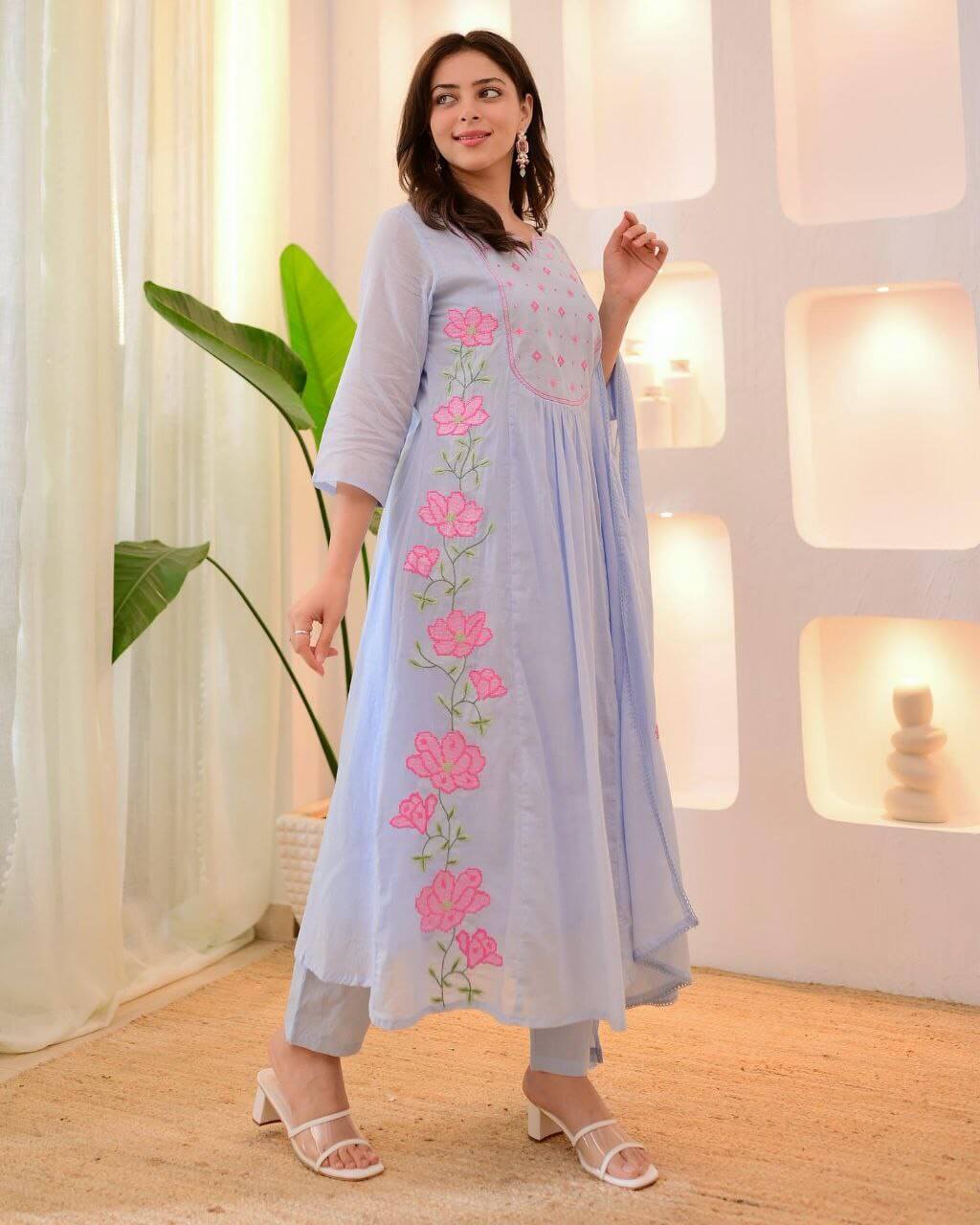 Woman wearing a light blue dress with pink floral embroidery in a bright room.