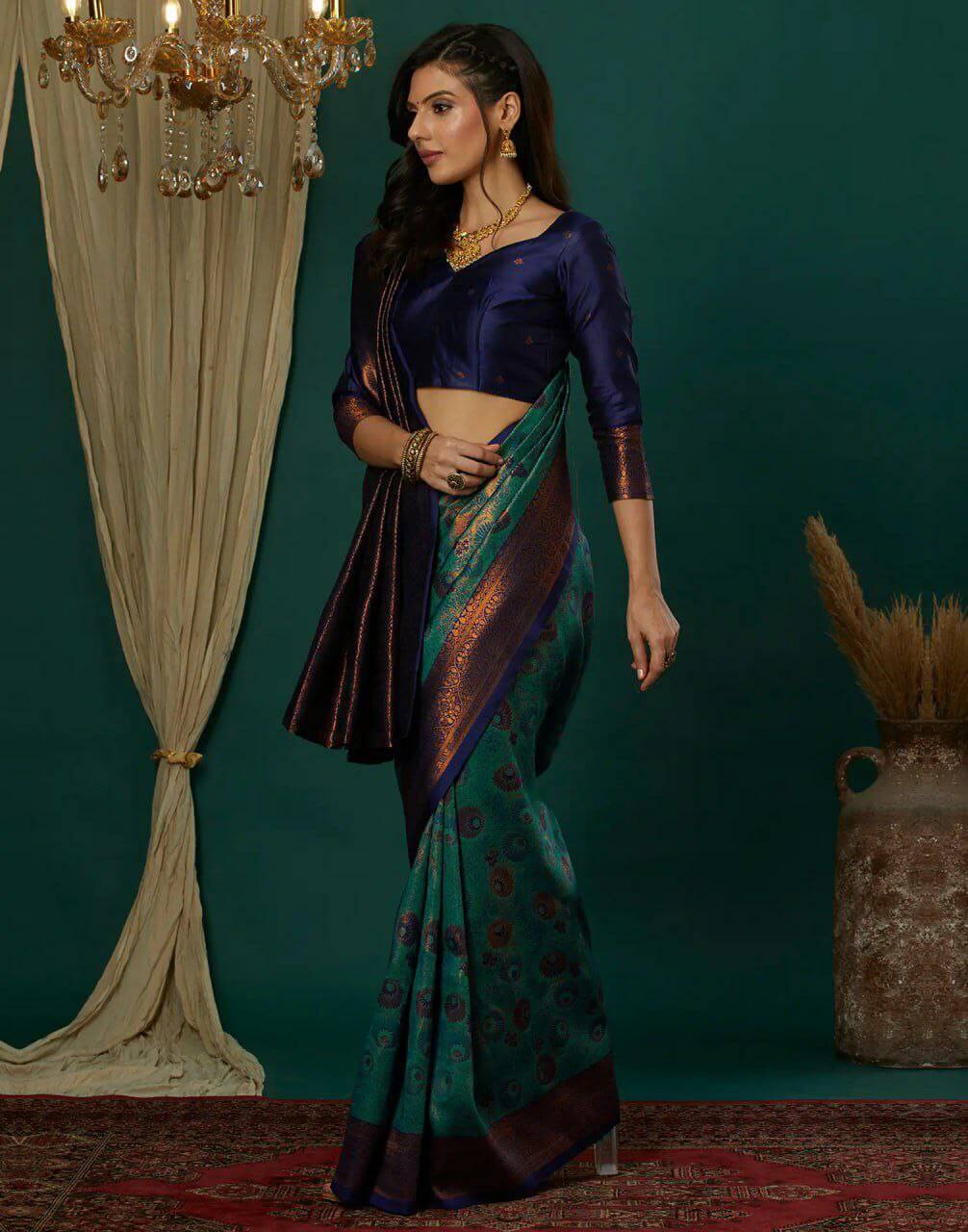 Woman in a traditional saree standing in a decorated room with a chandelier and curtains.